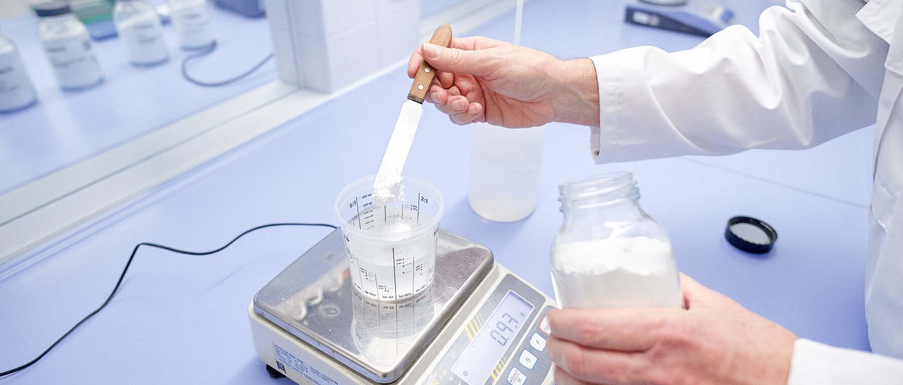 Employee weighs powder with a spatula and stirs it into a chemical liquid