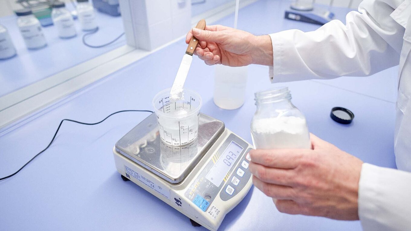 Employee weighs powder with a spatula and stirs it into a chemical liquid