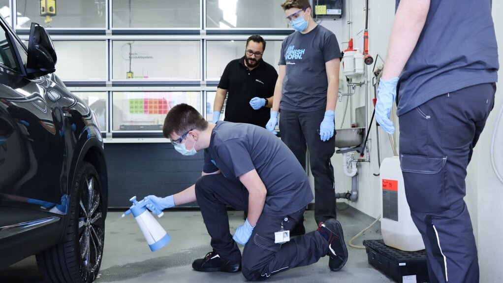 Employee showing an apprentice how to apply a Koch-Chemie product on a car’s engine hood with a polishing machine