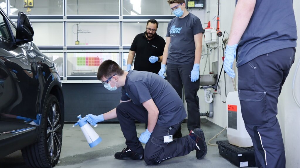 Employee showing an apprentice how to apply a Koch-Chemie product on a car’s engine hood with a polishing machine