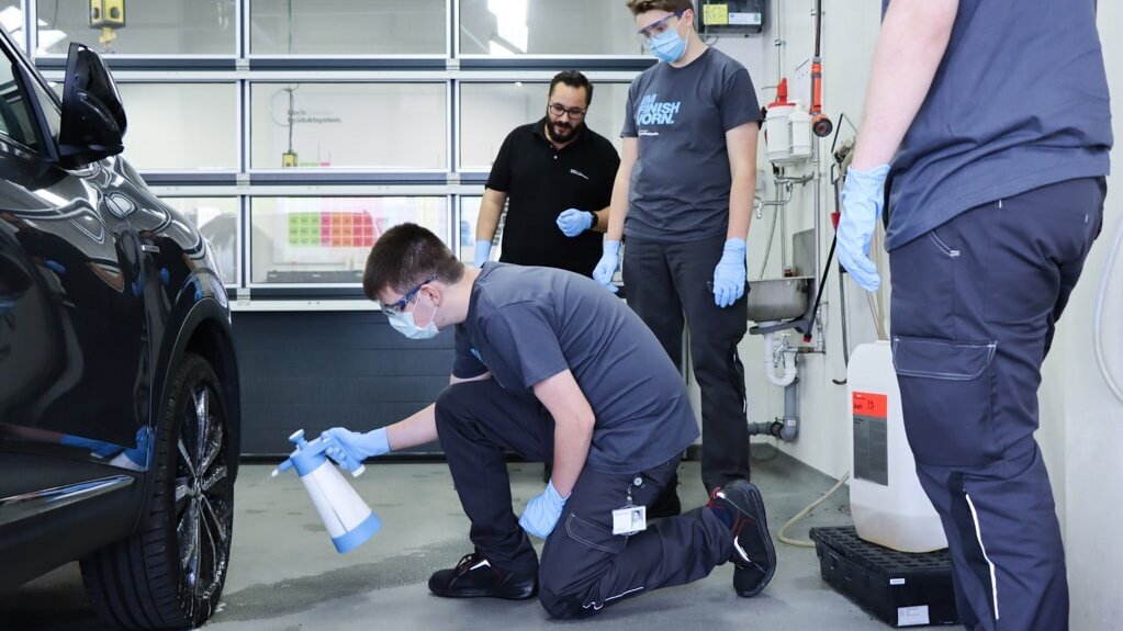 Employee showing an apprentice how to apply a Koch-Chemie product on a car’s engine hood with a polishing machine