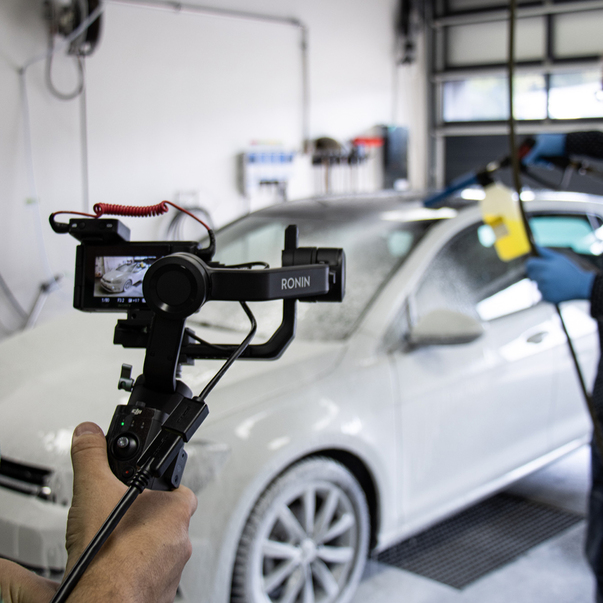 Camera man filming a white car being cleaned by an employee
