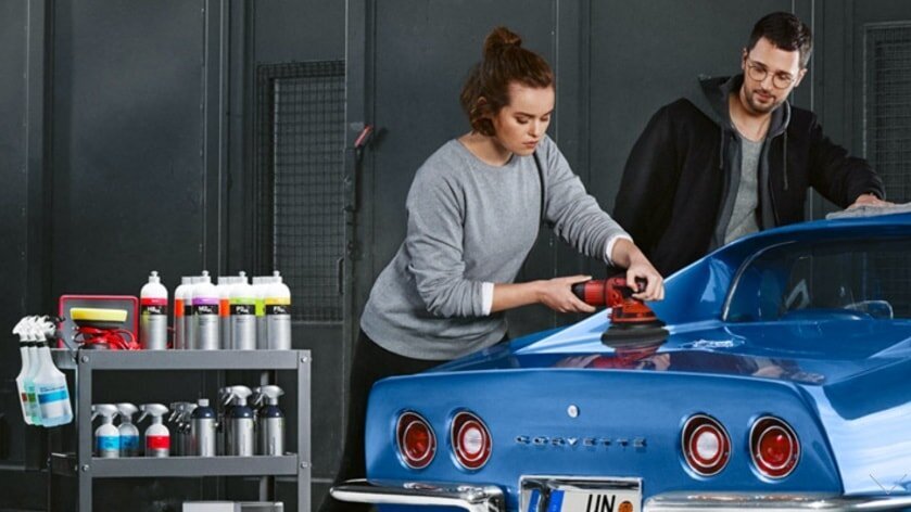 Woman polishing a blue sports car with a polishing machine with a man standing nearby