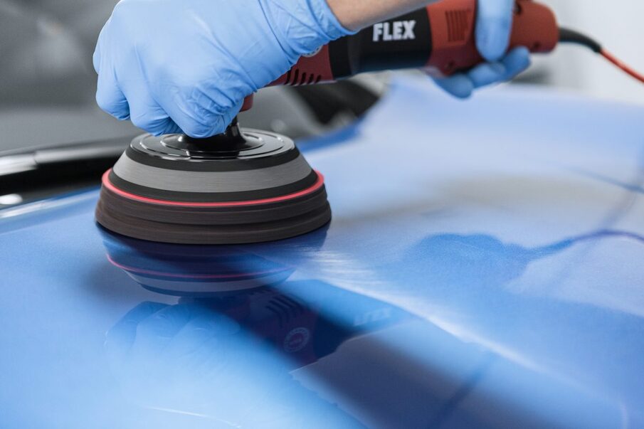 Close-up of a hand polishing a blue engine hood with a polishing machine