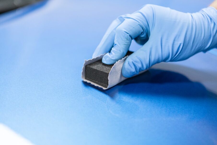 Close-up of a hand with a blue glove grinding a blue surface