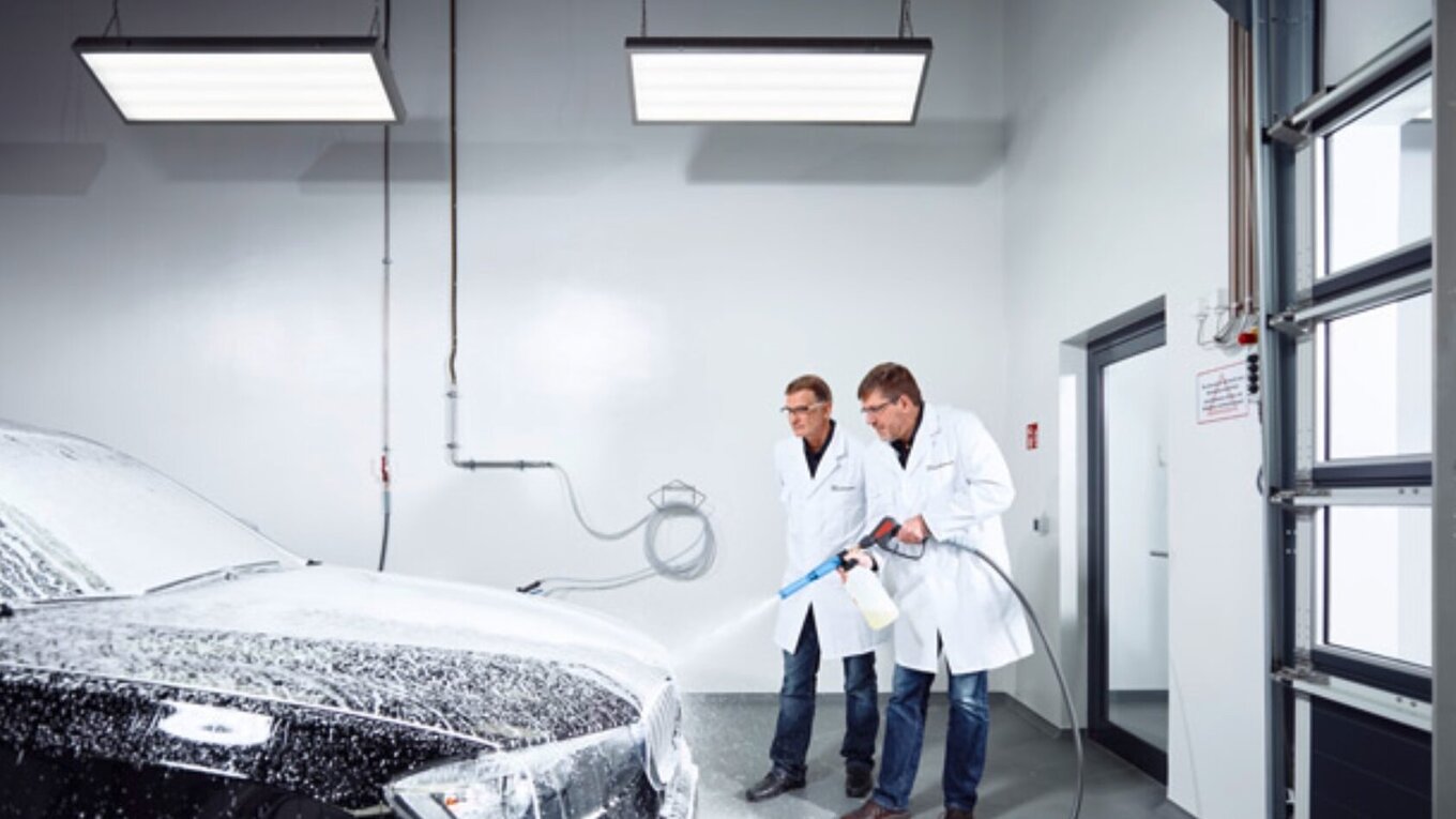 Employees foaming a black car with a high pressure cleaner in the CompetenceCenter